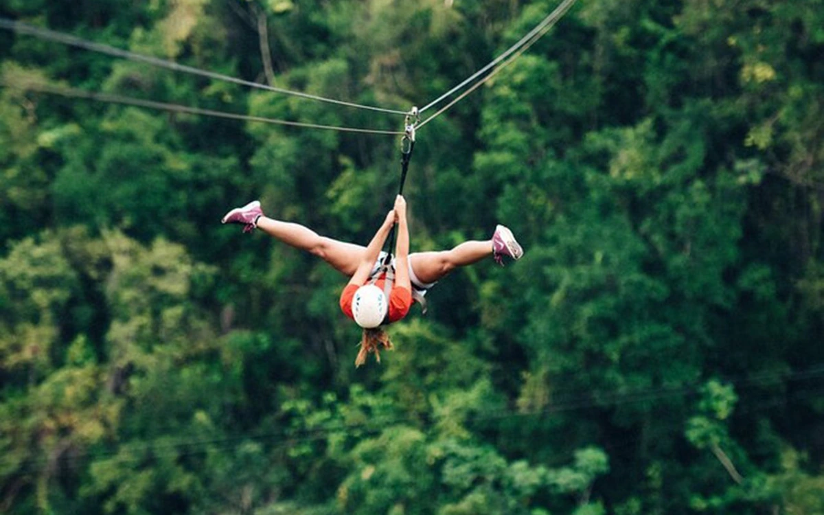 Ein Fahrer hängt kopfüber an einer Zipline-Rolle über dunkelgrünem Wald